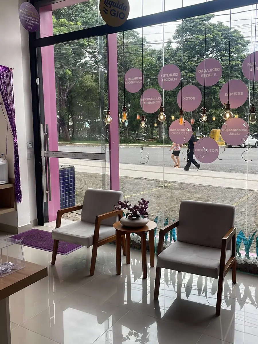 Recepção da GIO Jardim Suzana com poltronas, mesa com flores e vitrine voltada para a avenida